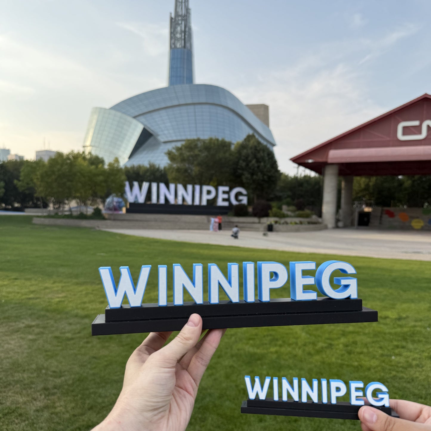 Person holding a 'Winnipeg' sign with the city hall in the background